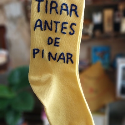 Meia amarela com texto bordado azul segura por mão em ambiente interior