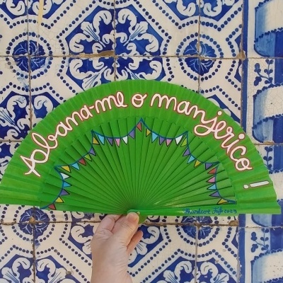 Ventoinha verde com texto rosa segurada em frente a azulejos azuis e brancos com padrões florais