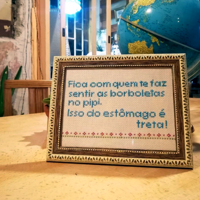 Quadro bordado com texto em português dentro de moldura dourada em mesa de madeira junto a um globo terrestre azul.
