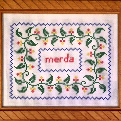 Quadro bordado com folhas, flores e a palavra 'merda' em vermelho
