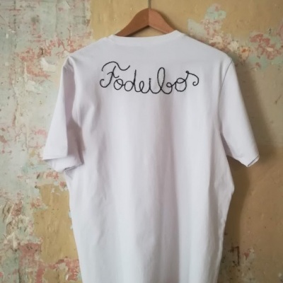 Camiseta branca de algodão com texto preto nas costas pendurada em cabide de madeira