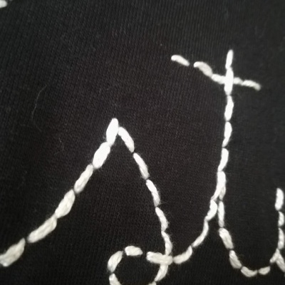 Tecido preto com bordado branco em linha formando letras cursivas