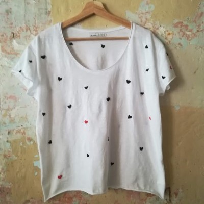 T-shirt branca com corações pretos e vermelhos pendurada em cabide de madeira