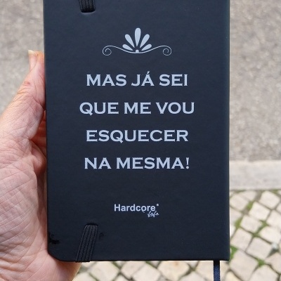 Caderno preto com texto branco, fita elástica e marcadora, segurado à mão