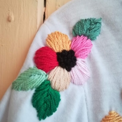 Bordado de flor colorida em tecido branco com folhas verdes e fundo de madeira clara