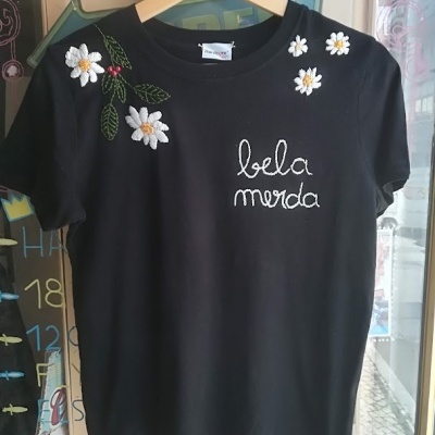 T-shirt preta bordada com flores brancas e texto 'bela merda'