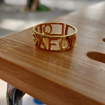 Anel dourado com letras recortadas numa superfície de madeira clara.