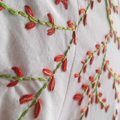 Tecido branco bordado com flores vermelhas e folhas verdes