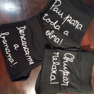 Três t-shirts pretas com inscrições em branco dobradas sobre madeira.