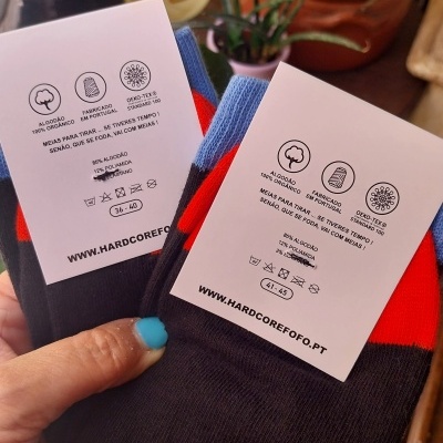 Duas meias pretas com vermelho e azul com etiquetas brancas e texto em português.