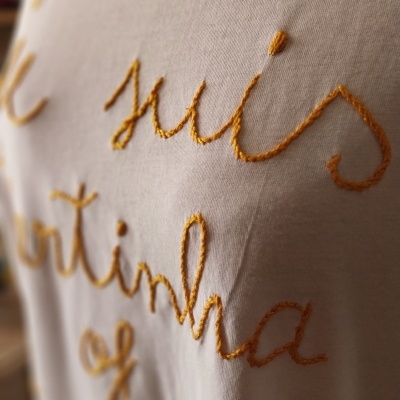 Tecido branco com bordado laranja em estilo cursivo