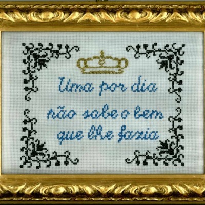 Quadro bordado com texto em azul e decoração preta e dourada numa moldura dourada