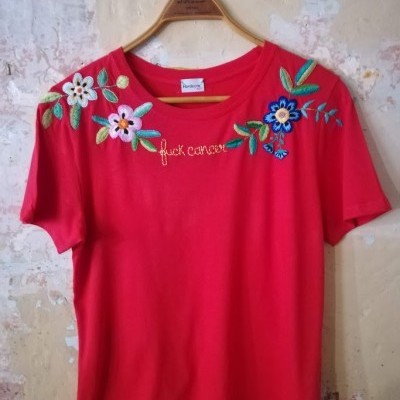 T-shirt vermelha de manga curta com bordados de flores e texto bordado 'fuck cancer'.