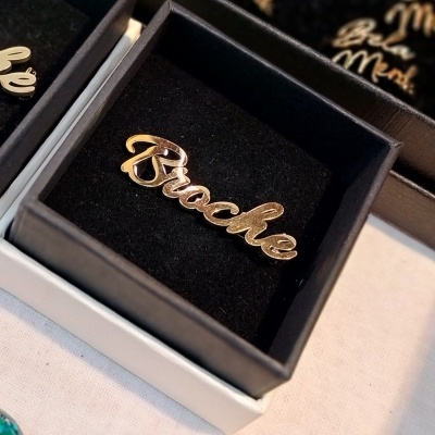 Anel dourado com palavra 'Brooke' em caixa preta aveludada