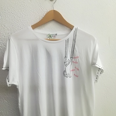 T-shirt branca com bordado de gato pendurado e texto 'FUCK' repetido em vermelho