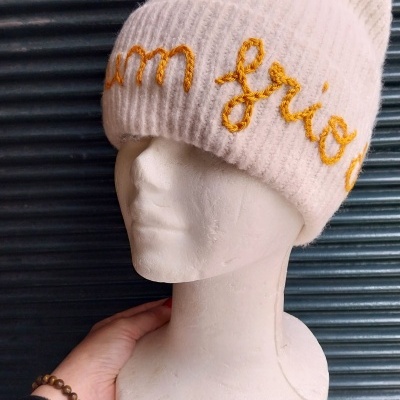 Gorro branco de malha com bordado amarelo numa cabeça de manequim branca