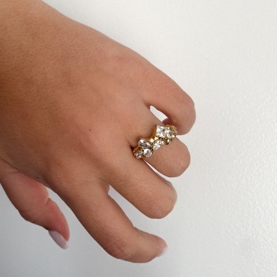 Mão com anel dourado e pedras transparentes em fundo branco