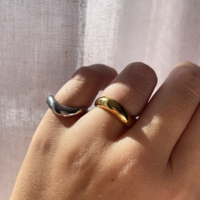 Anéis prateado e dourado em dedos com cortina clara ao fundo