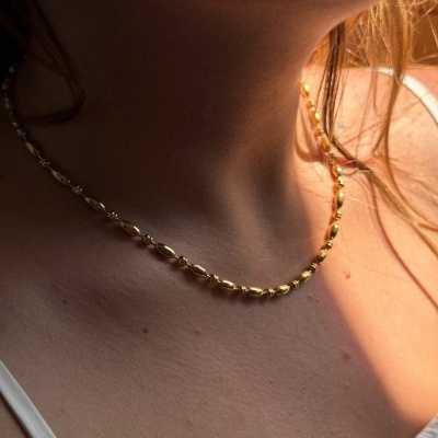 Colar dourado curto com elos texturizados no pescoço