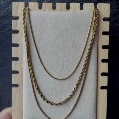 Três colares dourados em fundo bege com suporte de madeira