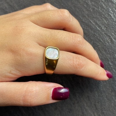 Anel de metal dourado com pedra clara usado no dedo médio em mão com unhas vinho