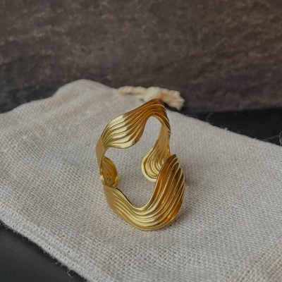 Anel dourado com design ondulado sobre saco de tecido cru