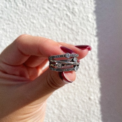 Anel prateado com pedras claras segurado por mão com unhas bordô