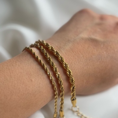 Pulseira de corrente dourada em metal com padrão torcido no pulso