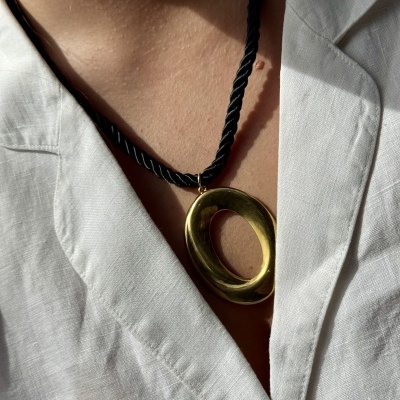 Colar com pendente oval dourado em cordão preto trançado ao pescoço com camisa branca