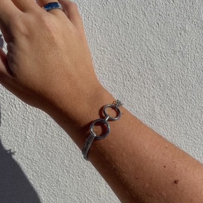 Pulseira e anel em metal prateado numa mão contra fundo branco