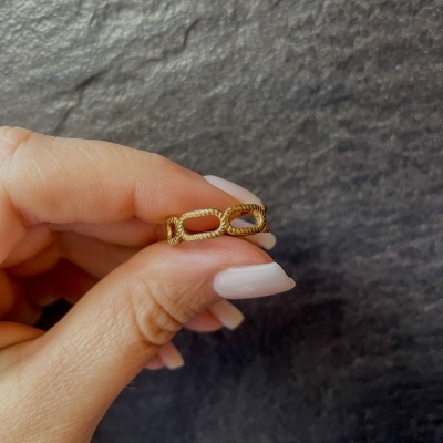 Anel dourado com formato de elos de corrente segurado pela mão