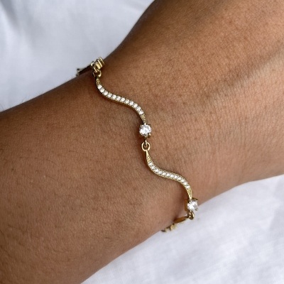 Pulseira dourada ondulada com pedras transparentes num pulso