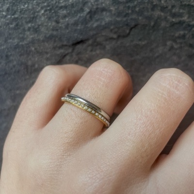 Anel bicolor com pérolas numa mão sobre fundo cinzento