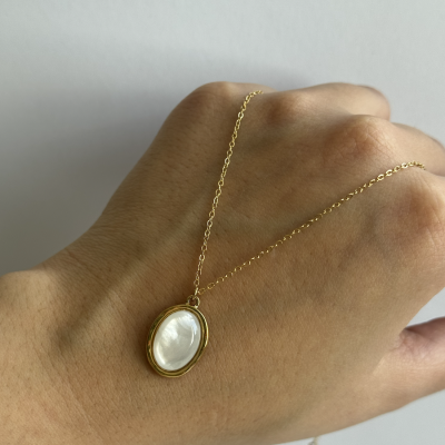 Colar dourado com pedra branca oval sobre mão