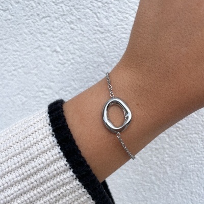 Pulseira fina prateada com pendente oval irregular num pulso com manga de camisola