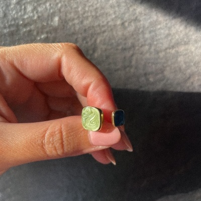 Anel aberto com pedras quadradas em verde e azul, em fundo cinza texturizado