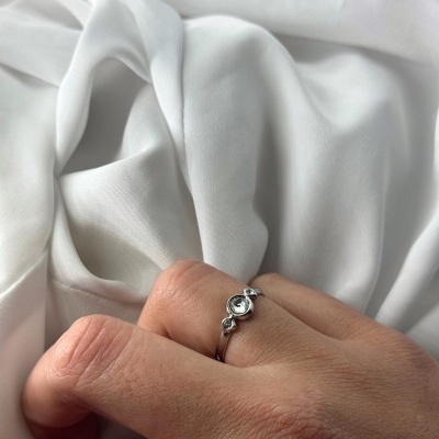 Anel prateado com pedra em mão sobre tecido branco