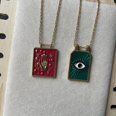 Dois colares com pendentes retangulares coloridos em fundo vermelho e verde exibidos em suporte de madeira