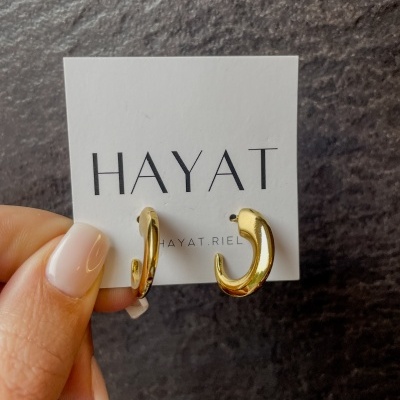 Brincos dourados em cartão branco com texto HAYAT.