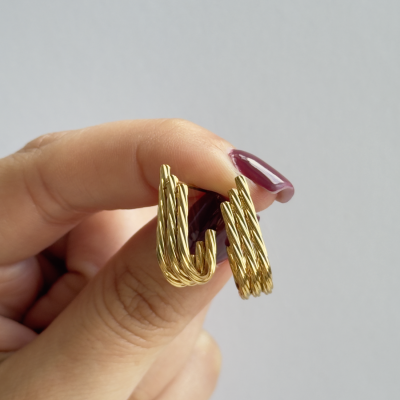 Brincos de argola dourados retorcidos segurados por mãos femininas com unhas pintadas de vinho