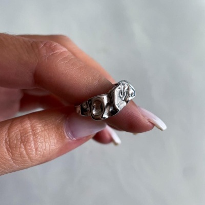 Anel prateado ondulado com gravações em relevo segurado por mão com unhas brancas