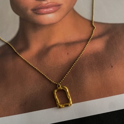 Colar dourado com pendente retangular sobre imagem de modelo