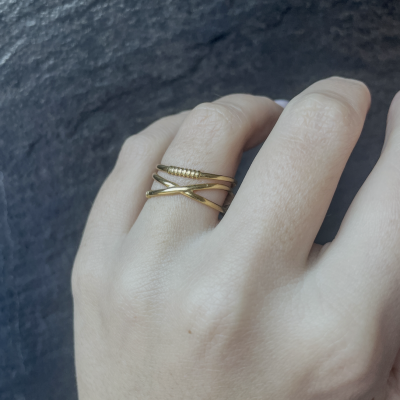 Mão com anel dourado cruzado detalhe esférico em fundo cinza escuro