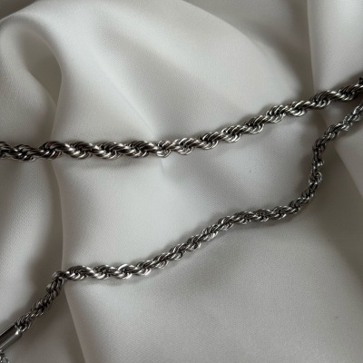 Colar ou pulseira de corrente metálica prateada com elos trançados sobre tecido branco