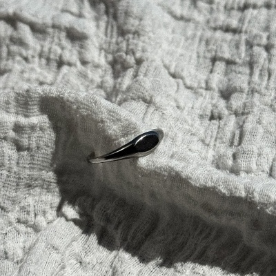 Anel prateado com pedra preta sobre tecido cinzento texturizado