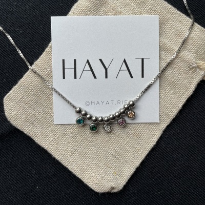 Colar prateado com pendentes coloridos sobre cartão branco e bolsa de tecido