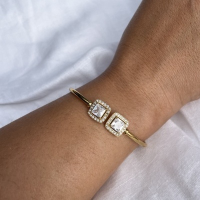 Pulseira dourada com pedras quadradas cristalinas no pulso sobre tecido branco