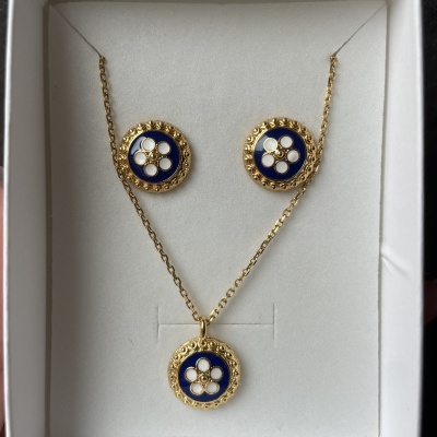 Conjunto de colar e brincos dourados com design azul e branco numa caixa branca