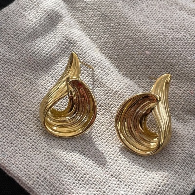 Brincos dourados curvos sobre tecido cinza claro texturizado