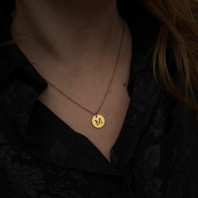 Colar dourado com pendente redondo letra M em pescoço